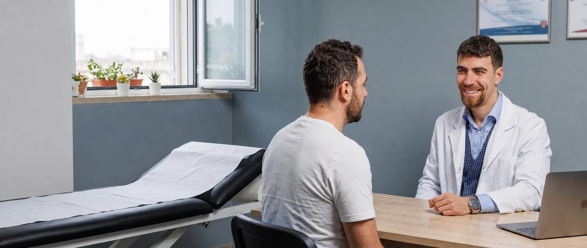 Il colloquio della prima visita: osteopata e paziente seduti alla scrivania, lo studio intero nel campo