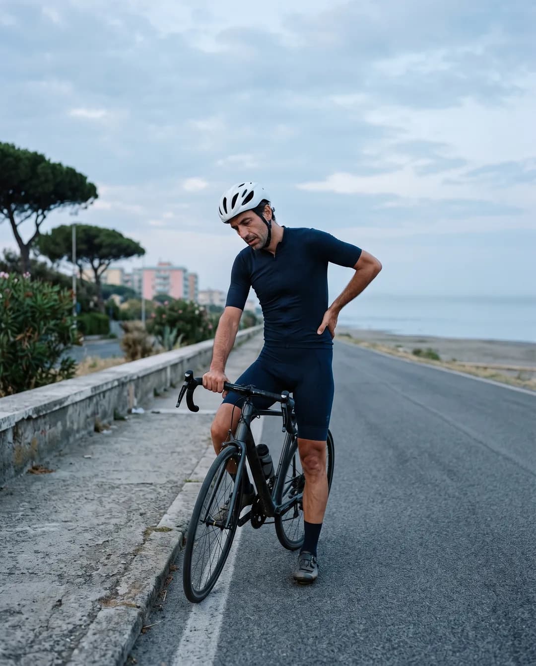 Un ciclista fermo sul lungomare si tocca la parte bassa della schiena